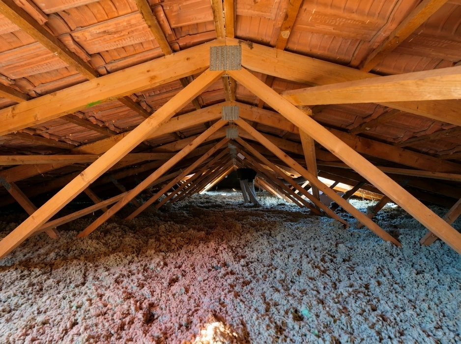 Intérieur de combles aménagés avec isolation en vrac par soufflage, composée de laine minérale (fibre de verre) rose et grise recouvrant le plancher entre les solives