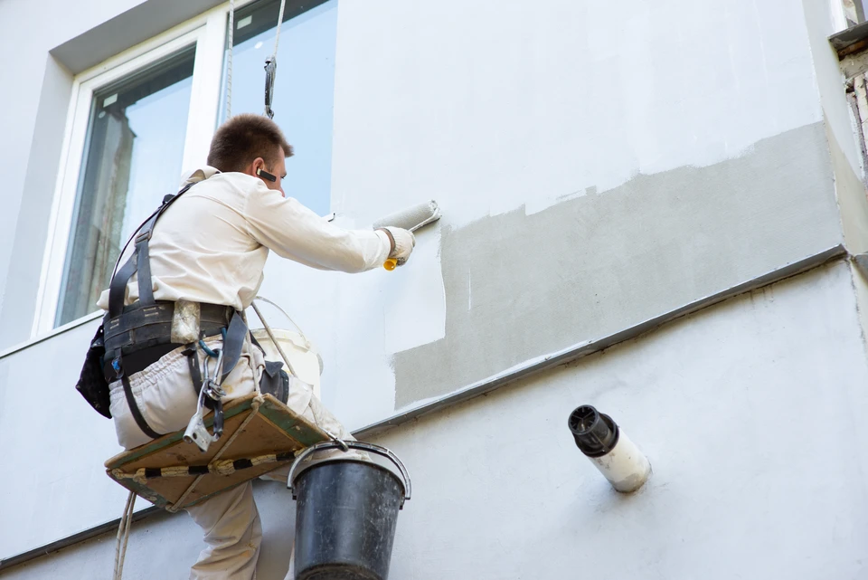 Ouvrier en combinaison blanche applique de la peinture au rouleau sur façade extérieure d'immeuble