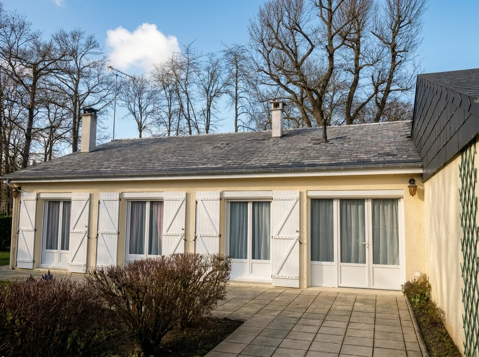 Pavillon de plain-pied style français, façade enduit beige, toiture en ardoise grise à faible pente avec deux souches de cheminée
