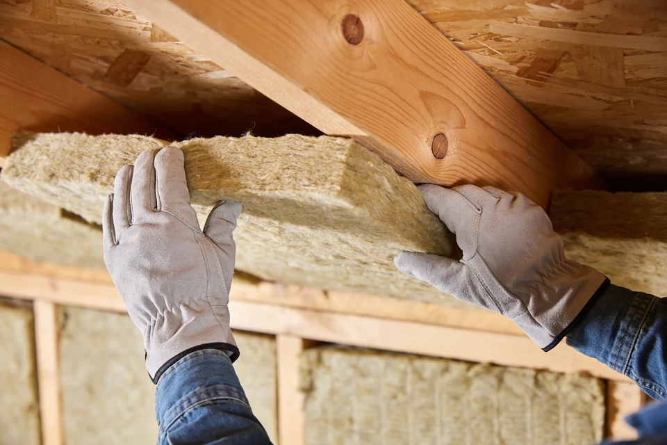 Main tenant avec gant vert appliquant un produit de protection sur planches de bois avec pinceau plat