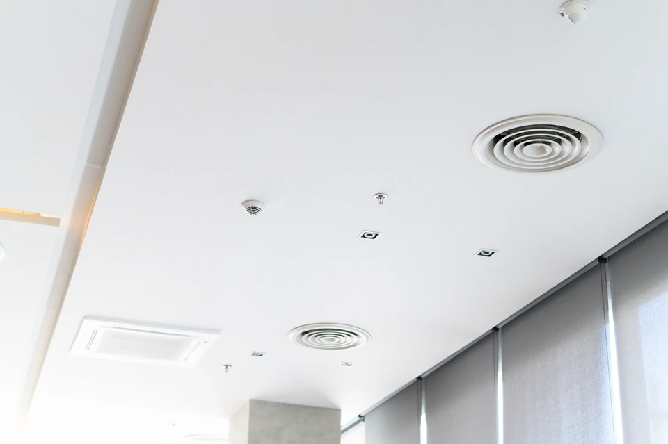 Un technicien en tenue de travail bleue installe des conduits de ventilation dans un local technique